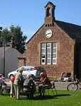 A small group of people at a picnic table outside the village hall.